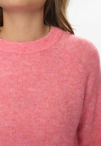 Pulover s puloverjem iz mehkega, mešanega rožnatega blaga. Ima rebrast krožni izrez, raglan rokave in prijetno teksturo brez vzorcev.
