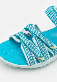 Sandal desportivo turquesa com tiras ajustáveis estampadas, detalhes brancos, palmilha texturizada e sola de borracha para tração.