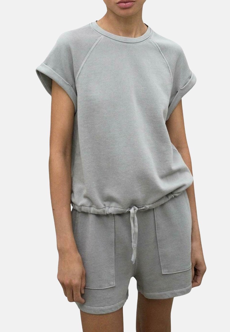 Salopette en mélange de coton gris clair avec des manches courtes, un col rond, une taille élastique avec cordon de serrage et deux poches avant. Texture douce, design décontracté.