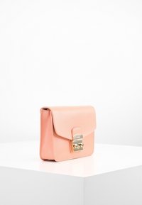 Różowa torebka ze skóry o wyraźnej, usztywnionej formie, zamykana na klapę, z dodatkami w kolorze złota. Gładka tekstura z delikatnym ziarnistym wzorem.