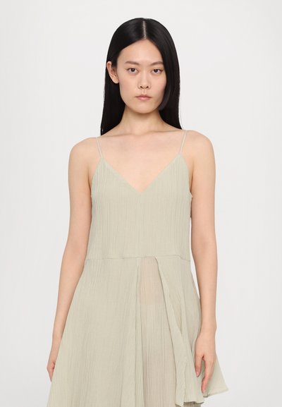 Light green sleeveless dress with a V-neckline, pleated texture, and an asymmetrical hem that flows gently. Adjustable thin straps.