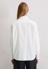 Biała, długosleeve, koszula zapinana na guziki o miękkiej fakturze, z klasycznym kołnierzykiem i prostym dołem, noszona na ciemnych spodniach.