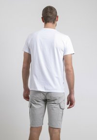 T-shirt en coton blanc à manches courtes, vue de dos, associée à un short cargo gris clair avec poches latérales et une coupe au niveau des genoux.