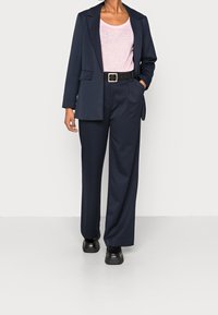 Navy blue tailored blazer paired with a light pink top and wide-leg navy trousers, accented with a black belt and chunky black shoes.