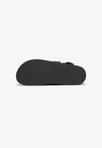 Svart sandal såle med en teksturert gummioverflate, med en konturert form og subtile merkevare detaljer. Minimalistisk design uten dekorasjoner.