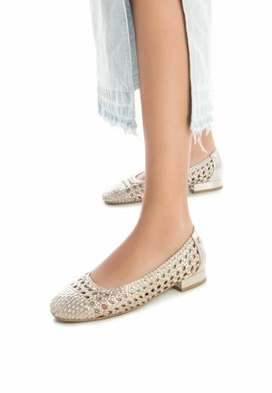 Los zapatos planos presentan un diseño de malla tejida en un color beige claro, con un tacón metálico brillante. La punta es redondeada, lo que proporciona un ajuste seguro.