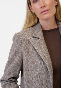 Brun kappa med fiskbensmönster och paljetter, skräddarsydd passform, slagkrage och en texturerad tyg, bärs över en enfärgad brun topp.