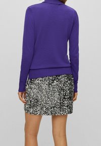 Top de manga larga morado con un cuello acanalado, combinado con una minifalda brillante de lentejuelas plateadas. Textura suave y diseño ajustado.