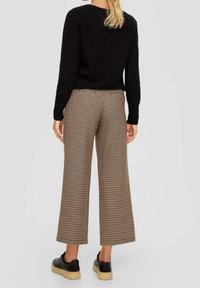 Pull noir en maille associé à un pantalon large marron à motif quadrillé et des chaussures à lacets noires avec une semelle beige. Aucun élément métallique ou accent visible.