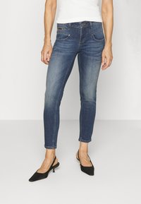 Mallas de mezclilla en azul oscuro con un ligero desvanecimiento, cinco bolsillos y un corte ajustado, combinadas con tacones negros tipo slingback.