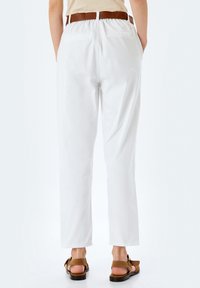 Pantaloni bianchi in cotone con vestibilità rilassata, caratterizzati da una cintura marrone e due tasche posteriori, abbinati a sandali marroni con cinturini.