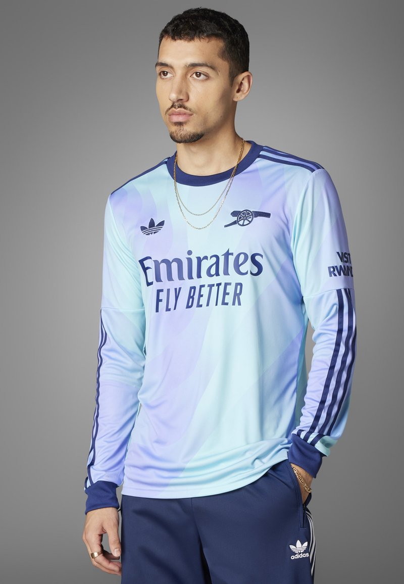 Lyseblå langærmet trøje har et gradientdesign, marineblå detaljer og "Emirates Fly Better" logo på forsiden. Adidas-striber på ærmerne.