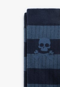Calcetines a rayas en azul marino y verde azulado, con un gráfico de calavera central. Textura de punto, puño acanalado, con tonos oscuros y claros contrastantes.