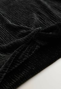 Schwarzer Samtstoff mit einem strukturierten gerippten Muster, das weiche, plüschige Fasern und eine glatte Oberfläche zeigt, gefaltet mit einem leichten Fall.