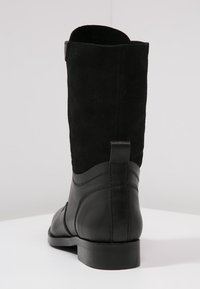 Botas negras hasta la rodilla que presentan una combinación de ante y cuero, con una textura suave y una abertura amplia en la parte superior.