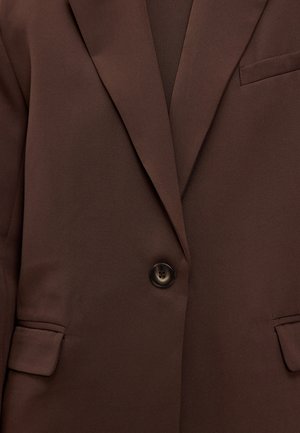 Blazer marron avec revers crantés, fermeture par un seul bouton foncé et poches à rabat de chaque côté.