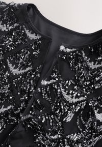 Zwarte top met ingewikkelde paillettenpatronen en -texturen. Voorzien van geometrische ontwerpen in glanzend zwart en zilver op een gladde achtergrond.