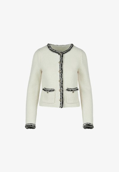 Krémkötésű kardigán fekete-fehér tweed díszítéssel, gyöngygombokkal és két elülső zsebből, fehér háttéren bemutatva.