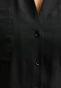 Zbliżenie czarnej koszuli zapinanej na guziki, zapiętej na guziki i z kieszenią na piersi po lewej stronie.