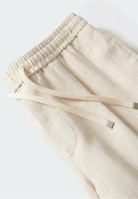 Beige linnen joggers met een elastische tailleband, voorzien van een trekkoord met metalen eindkappen en zijzakken. Glad textuur en casual ontwerp.