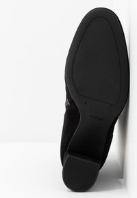 Semelle d'une bottine en daim noir avec un petit talon bloc, nom de la marque « högl » visible sur la semelle extérieure lisse.