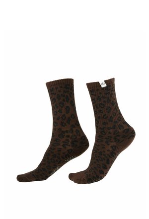 Par de calcetines marrones hasta la mitad de la pantorrilla con manchas de leopardo negras y puntos antideslizantes en las suelas, un calcetín etiquetado con una etiqueta blanca "clz".