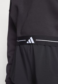 Zwart sporttopje met een aansluitend bovenstuk en een uitlopende onderkant. Voorzien van een contrasterend wit Adidas-logo en horizontale streepdetails.