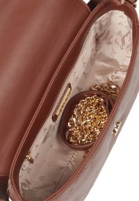 Brown leather handbag interior featuring a fabric lining with a logo pattern, gold chain, and a zippered pocket for small items.