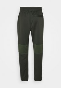 Pantalones deportivos de color verde oscuro con una textura suave, ajuste entallado y paneles de rodilla verdes en contraste. Cuentan con una cinturilla elástica y un bolsillo trasero.