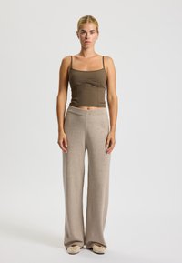 Brun tætsiddende tanktop og lyse beige brede strikbukser. Modellen står lige med ret ryg og viser begge beklædningsgenstande klart.