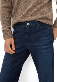 Jeans in denim blu scuro con vestibilità dritta, design a cinque tasche e chiusura con bottone in metallo. Il cinturino mostra sottili dettagli di cucitura.