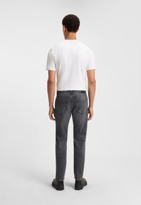 Jeans in denim grigio con una vestibilità slim, dotati di tasche posteriori e di una fascia in vita, abbinati a una t-shirt bianca a maniche corte.