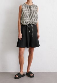 Hihaton toppi, jossa on beigejä ja mustia kukkakuvioita, yhdistetty polvipituiseen mustaan hameeseen ja mustiin punottuihin liukusandaaleihin.