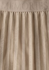 Beige pleated fabric with a textured pattern, where the word "MUISTOT" is embroidered across the top in a contrasting color.