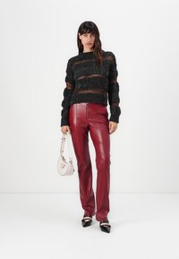 Chunky black knit sweater with orange stripes, paired with fitted red leather pants. Accessories include a small light pink handbag and black heels.