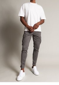 Witte katoenen t-shirt met een relaxte pasvorm, gecombineerd met slim-fit grijze cargobroeken met zijzakken, en witte sneakers.