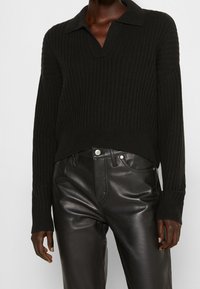 Suéter negro de punto acanalado con escote en V y cuello, combinado con pantalones de cuero negros. Presenta mangas largas y un diseño corto.