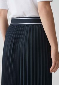 Jupe plissée marine avec une large taille élastique ornée de rayures blanches. La texture est lisse, mettant en valeur les plis réguliers tout au long.