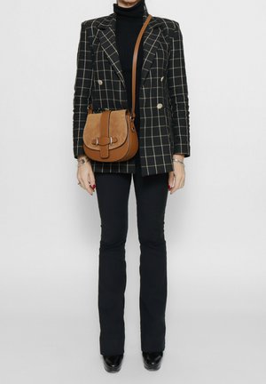 Schwarz-weißer kariierter Blazer mit goldenen Knöpfen, kombiniert mit einem schwarzen Rollkragenpullover und ausgestellten schwarzen Hosen. Braune Wildleder-Schultertasche.