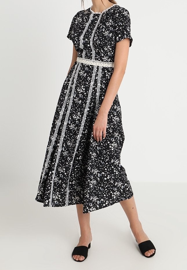 Svart blommig klänning med vita detaljer, korta ärmar och en figursydd midja. Tyget har en slät yta med små blommönster överallt.