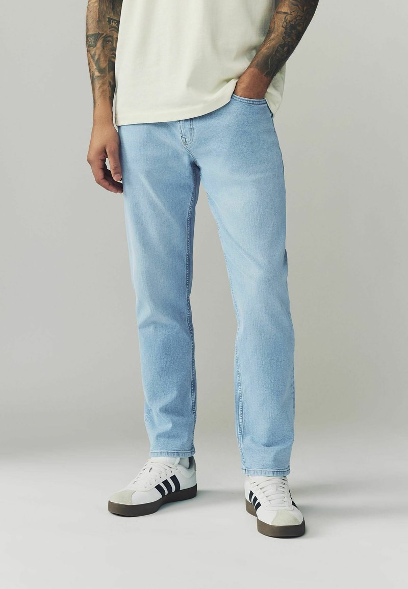 Jeans in denim azzurro chiaro con una vestibilità a gamba dritta, abbinati a sneaker bianche e nere. I jeans presentano una sottile texture e un design classico delle tasche.
