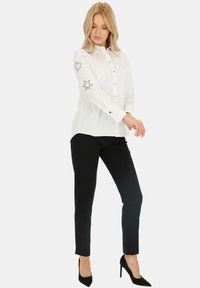 Biała koszula z guzikami, ozdobiona haftowanymi detalami w kształcie serca i gwiazdy na rękawach, zestawiona z czarnymi, dopasowanymi spodniami i czarnymi szpilkami.
