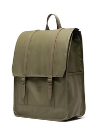 Zaino verde oliva realizzato in tessuto liscio con chiusura a patta, due cinghie frontali e un piccolo logo impresso sul pannello frontale inferiore.