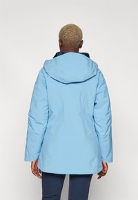 Giacca con cappuccio di un azzurro chiaro, dal tessuto liscio, con un interno blu scuro, maniche lunghe e una forma leggermente aderente.