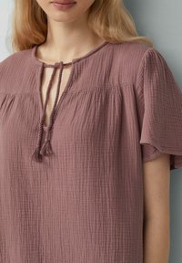 Rosa, strukturierte Bluse mit einem Schlüsselloch-Ausschnitt und Bindeband, mit kurzen Ärmeln und lockerer Passform. Hergestellt aus einem leichten Material.