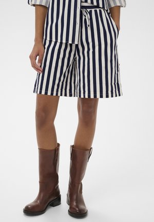 Pantaloni scurți din bumbac cu dungi în bleumarin și crem, cu talie elastică și buzunare. Asortați cu cizme maro din piele până la genunchi.