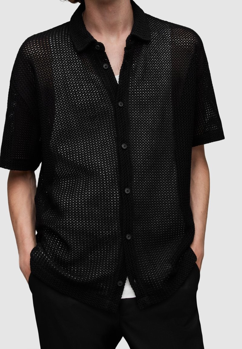 Camicetta nera a maniche corte con bottoni realizzata in tessuto a rete, con colletto e vestibilità ampia, caratterizzata da un design testurizzato a maglia aperta.