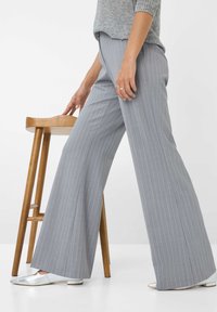 Grijze pantalon met een brede pijpdesign. De stof heeft een zachte textuur. Gecombineerd met zilveren puntige ballerina's en een houten kruk in de buurt.