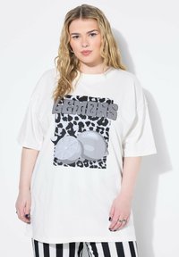 Camiseta blanca de gran tamaño con un gráfico en blanco y negro de estampado de leopardo y limones grises. El texto dice "LEMONS" en letras grandes.
