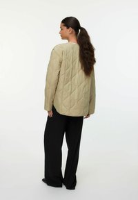 Lys beige quilted jakke med en afslappet pasform, der har en rund halsudskæring og lange ærmer, parret med sorte vide bukser.